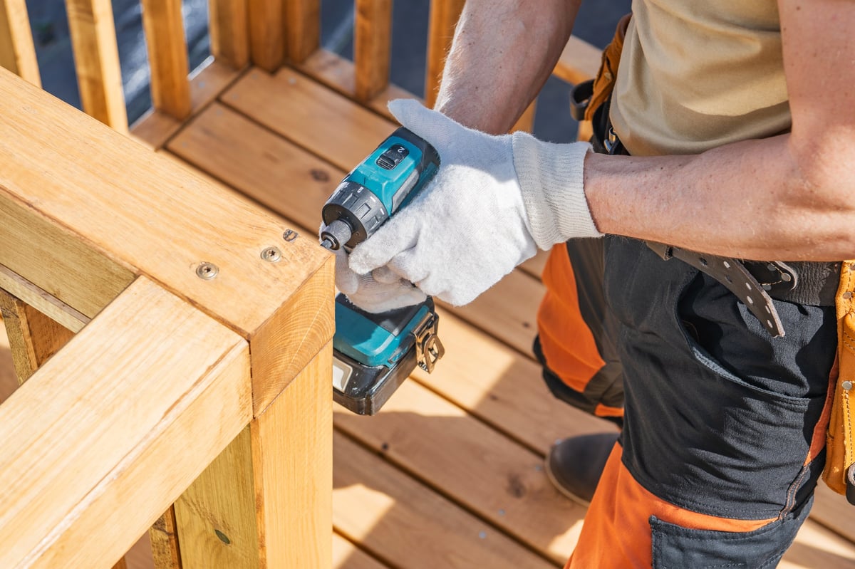 Worker securing a wooden fence railing with a cordless drill outdoors
